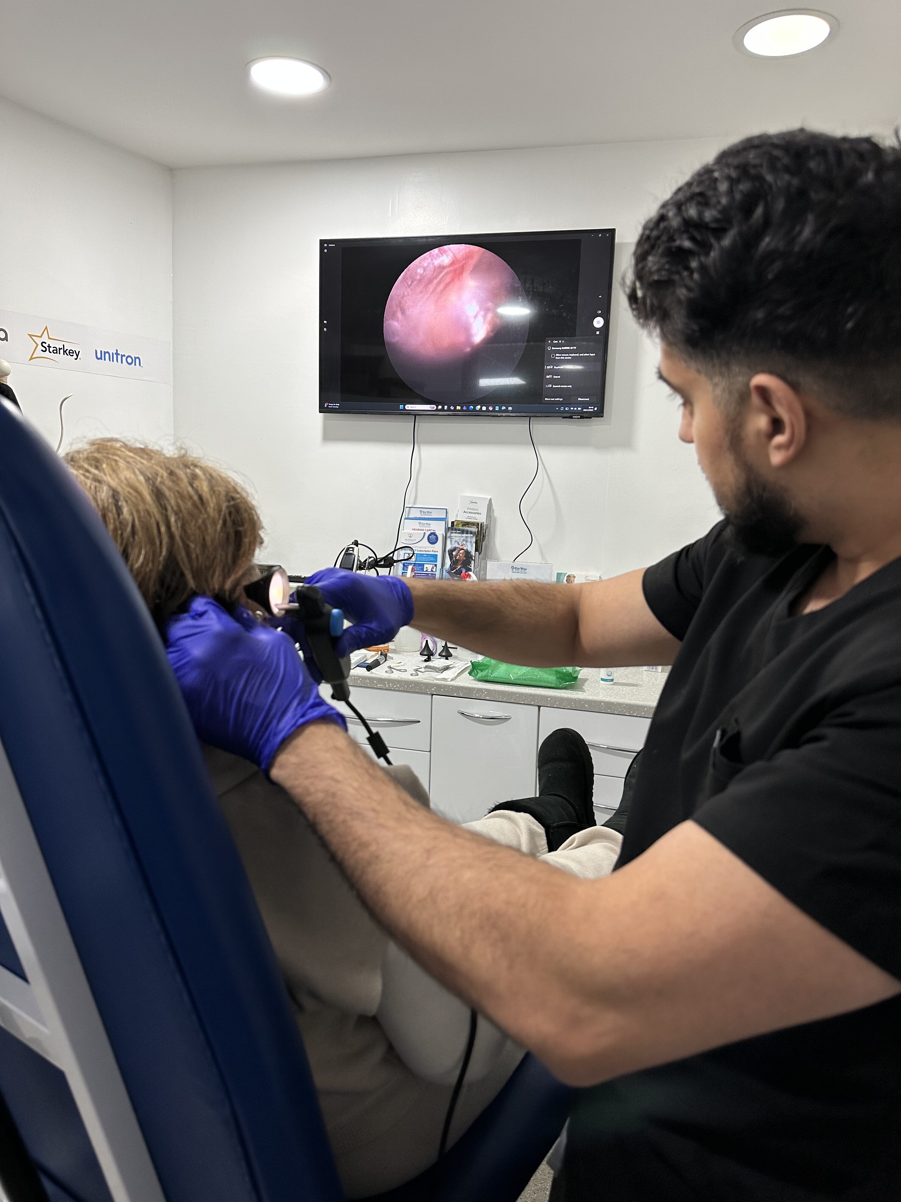 Specialist performing ear examination on a patient, with inner ear view on screen.